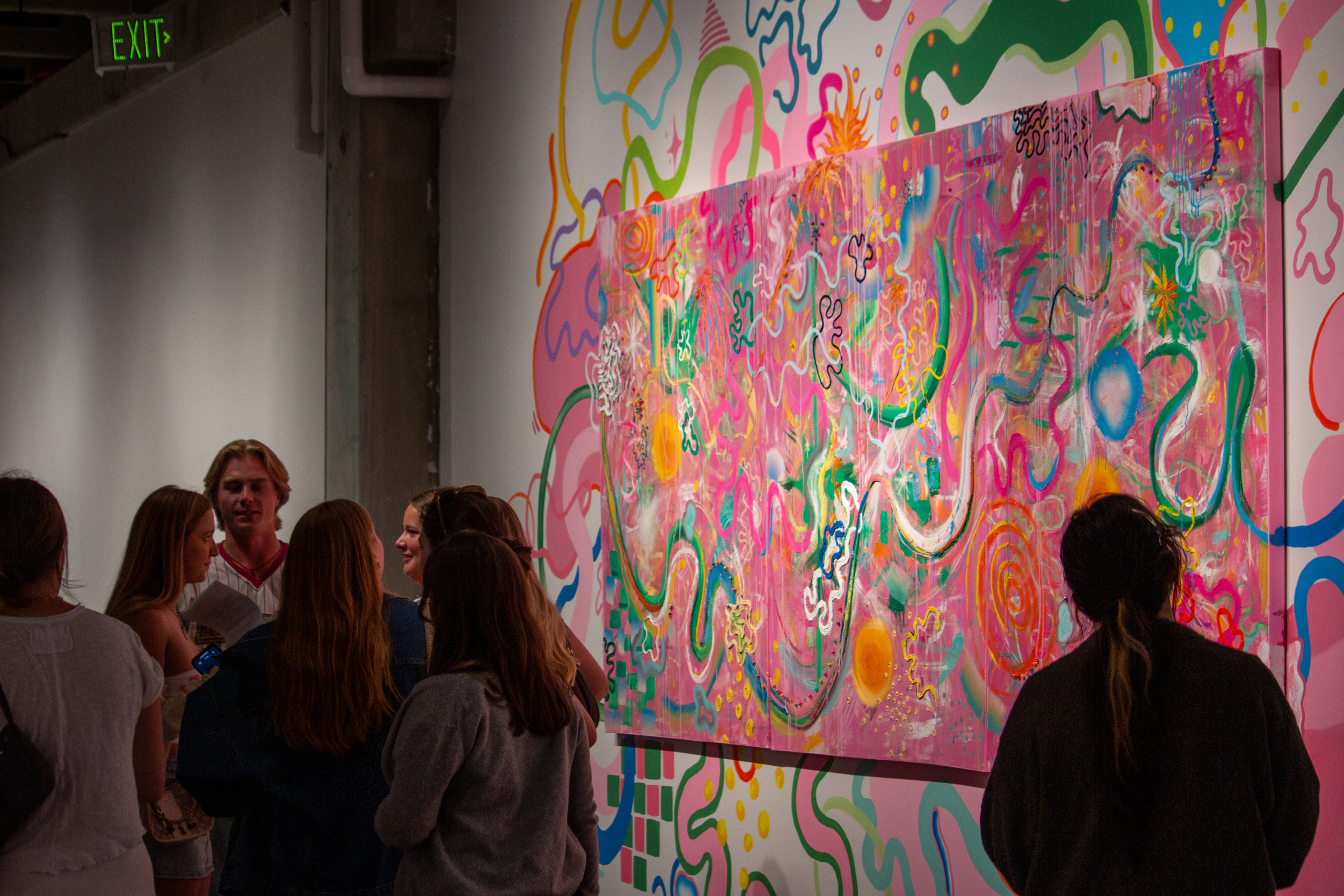 A group of DU students stand in front of a colorful painting and mural.
